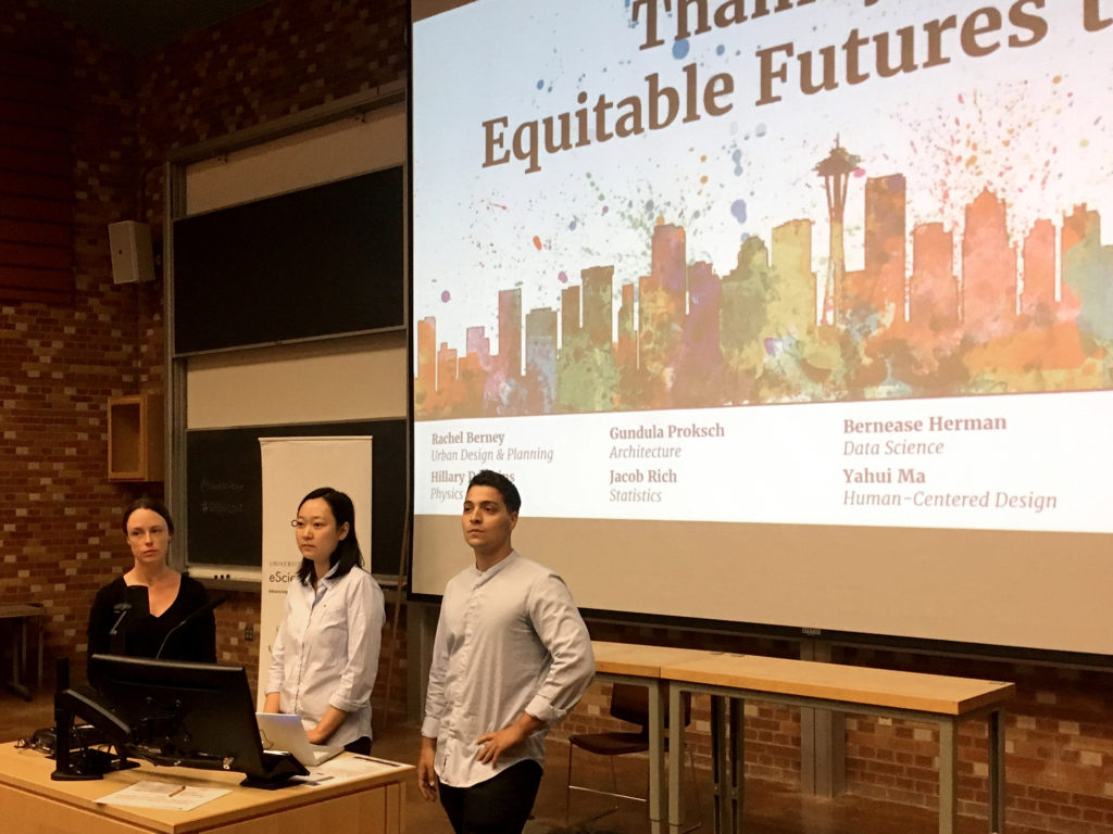 3 people standing in front of a powerpoint screen with a slide that says Equitable Futures