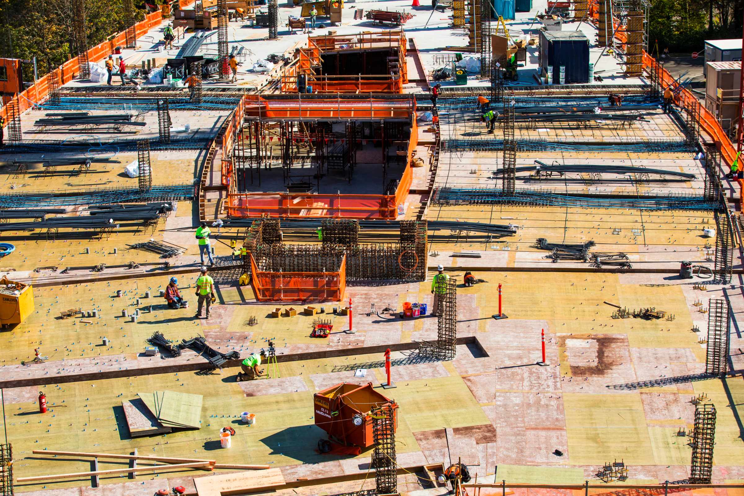 Aerial view of a construction site with workers, reinforcing steel structures, and wooden planks laying the foundation of a large building.