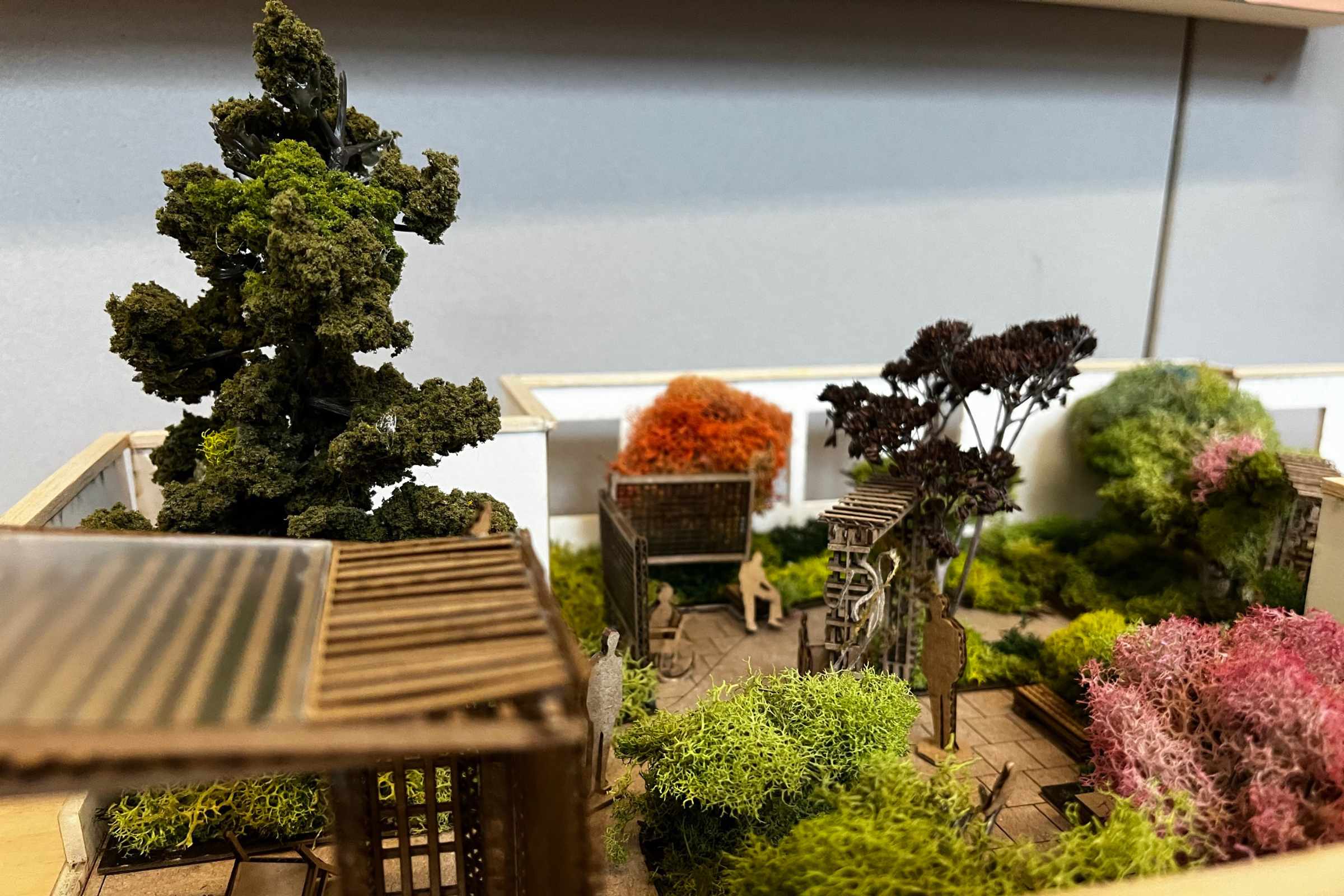 Close-up of an intricate architectural model featuring lush miniature trees, a gazebo, and detailed landscaping around modernistic structures.