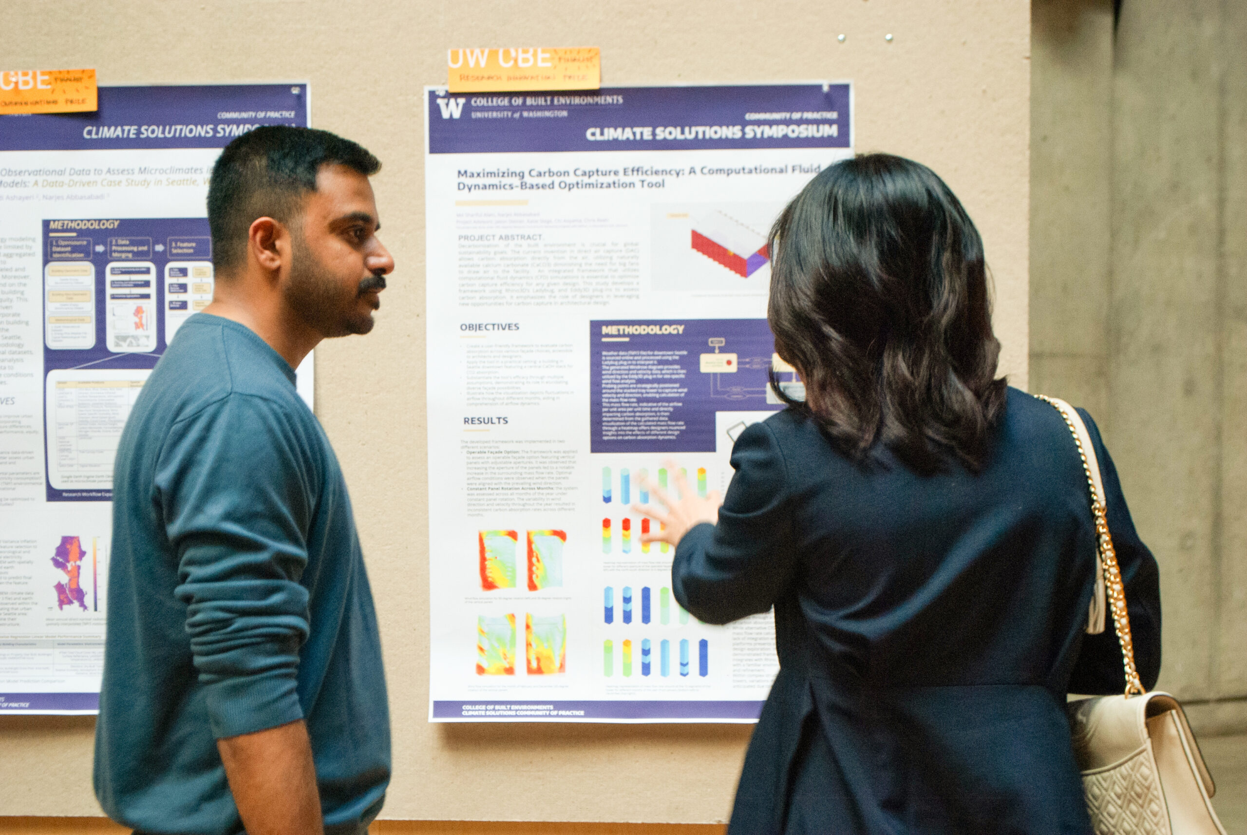 Student asking another student a question about their research presented on a poster in front of them.