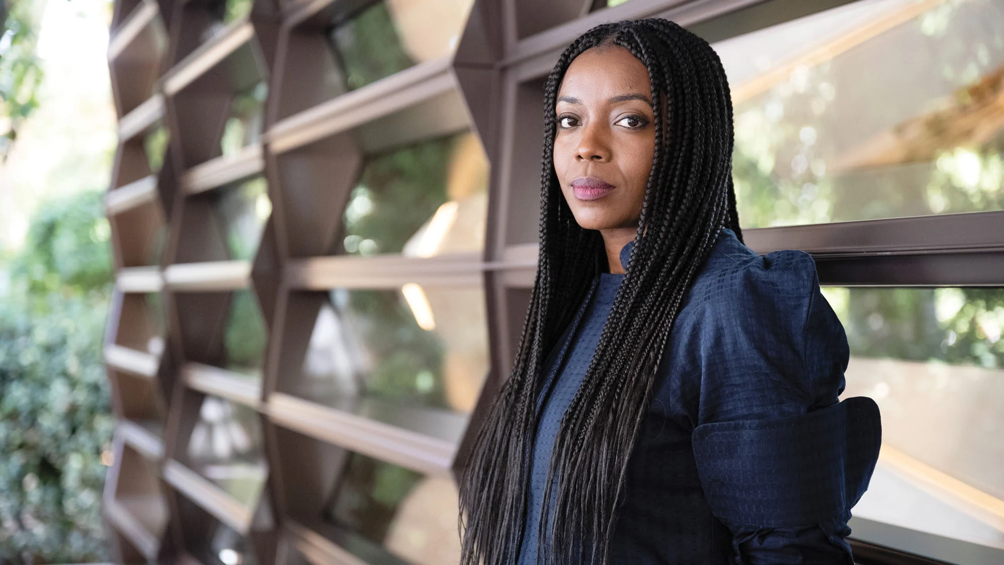 Woman with long dark hair dressed in black, leaning against a wall made of horizontal planks