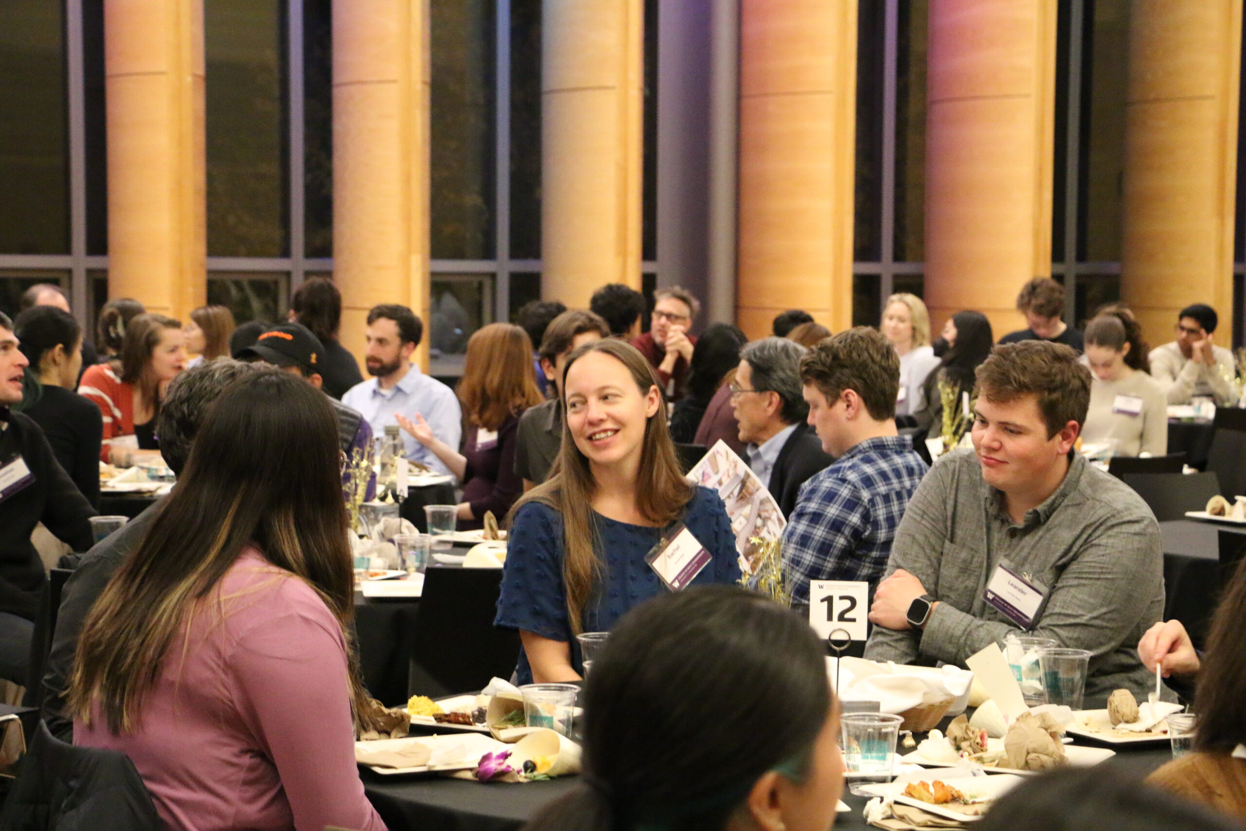 Student sitting with other students and mentors at a table in a crowded room