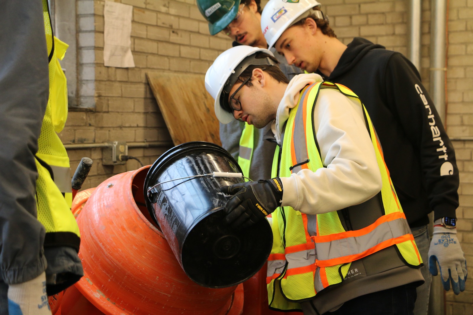 Student in construction gear pouring material into an orange cement mixer