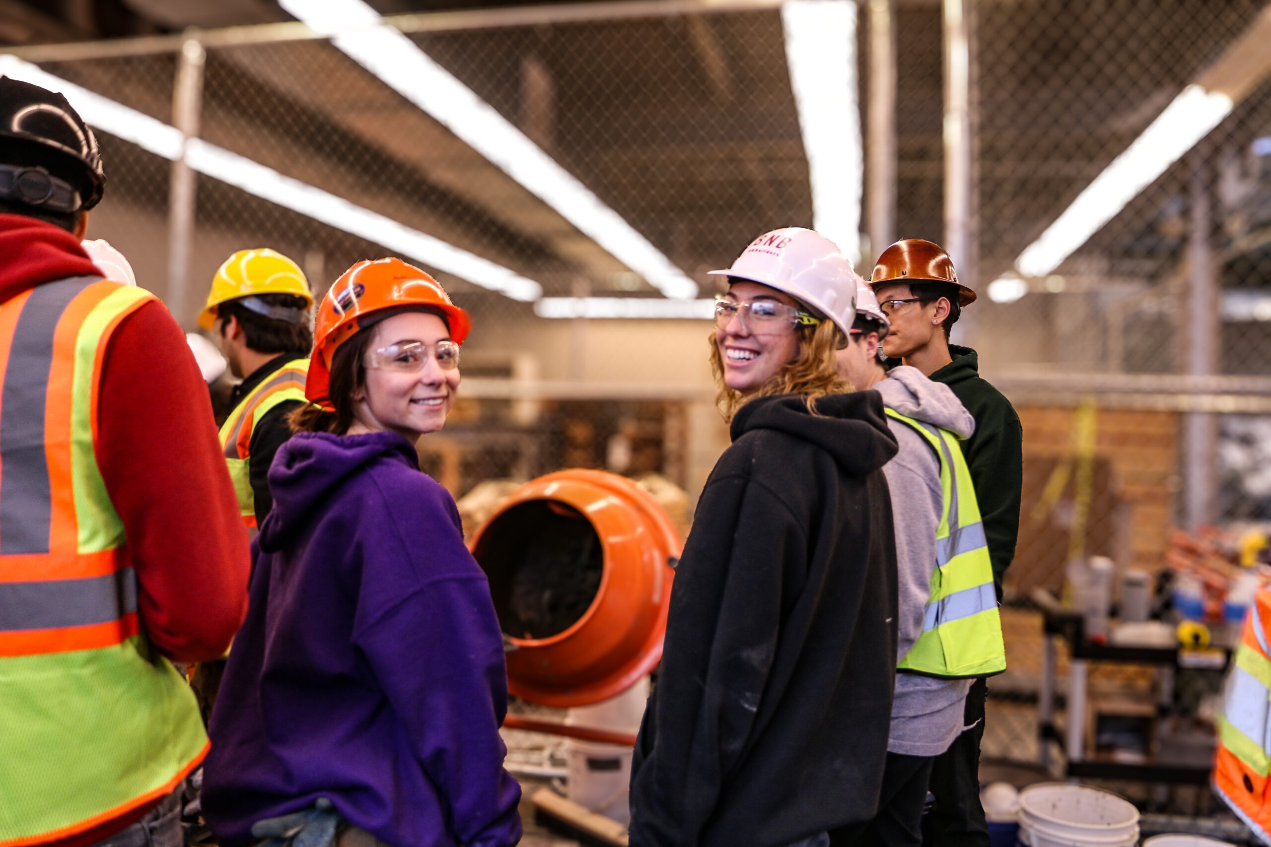 Two students in front of a concrete mixer turned and smiling at the camera
