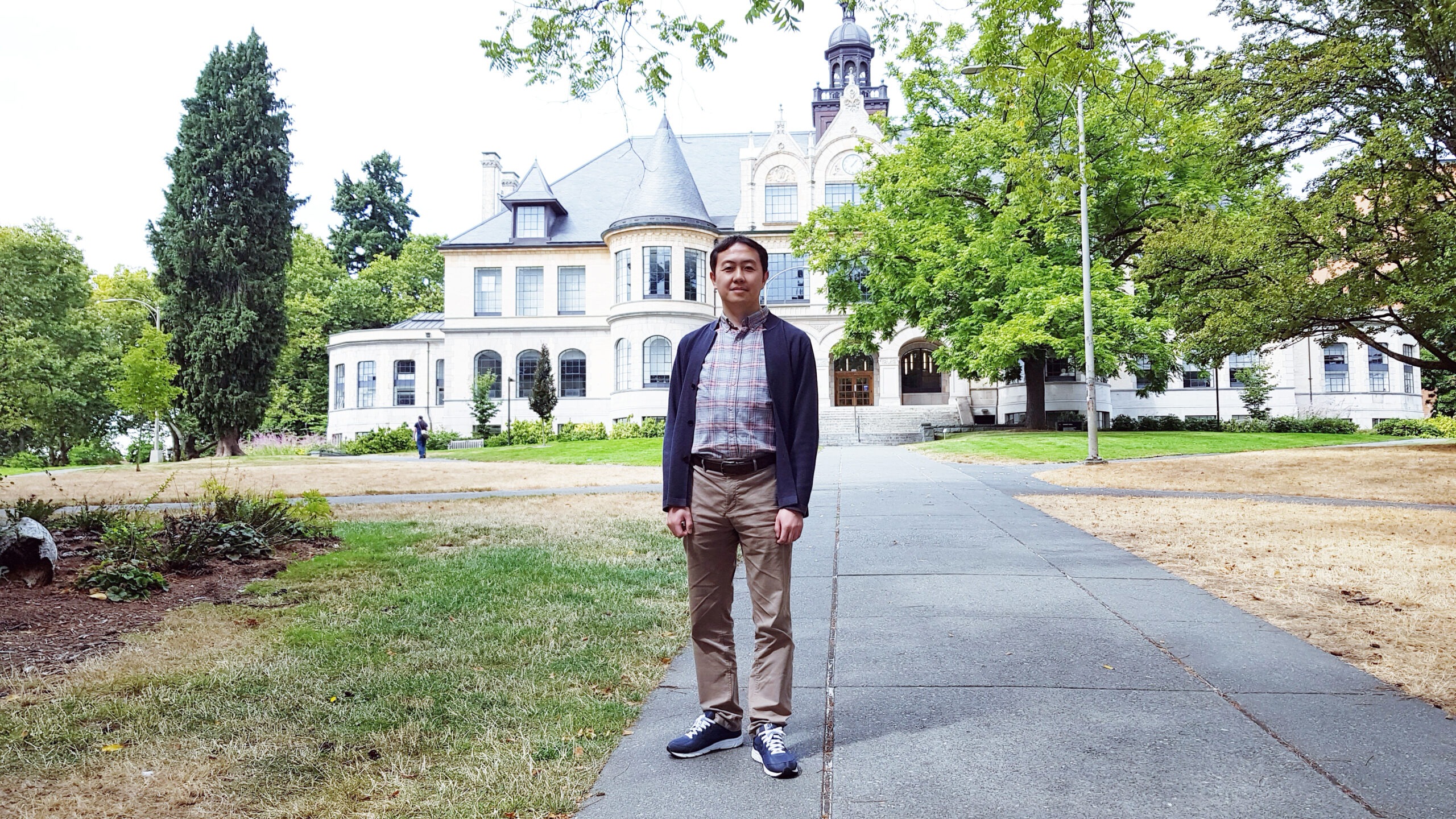 UDP visiting scholar Chung Ho standing on a path in front of a building on UW's campus