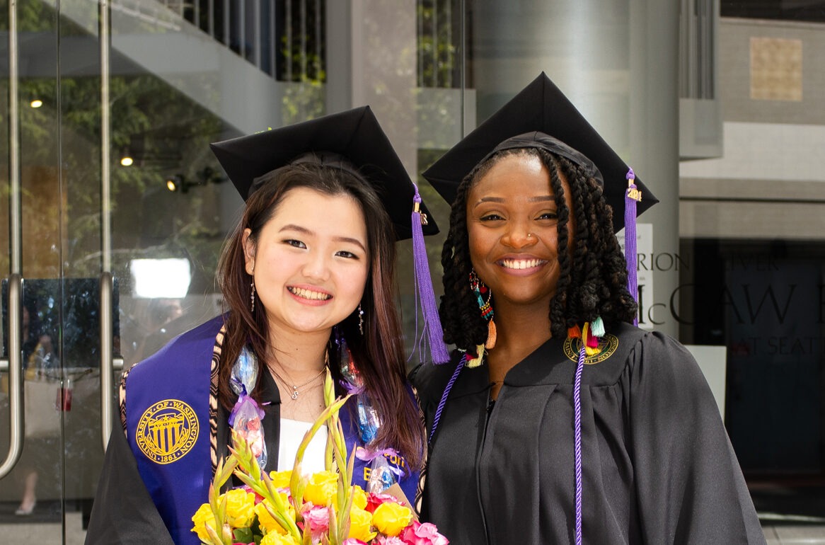 Two students in graduation attire smiling