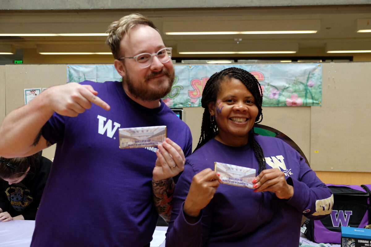 Two people smiling and pointing at chocolate bars that say College of Built Environments