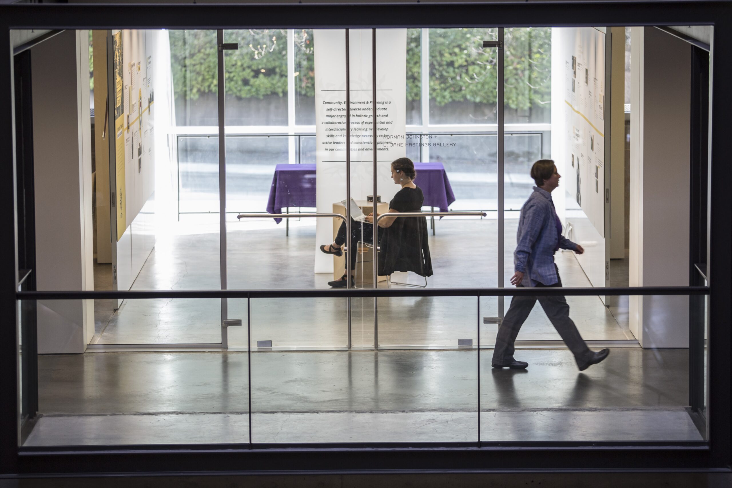 Person sitting in Gould Gallery with another person walking past