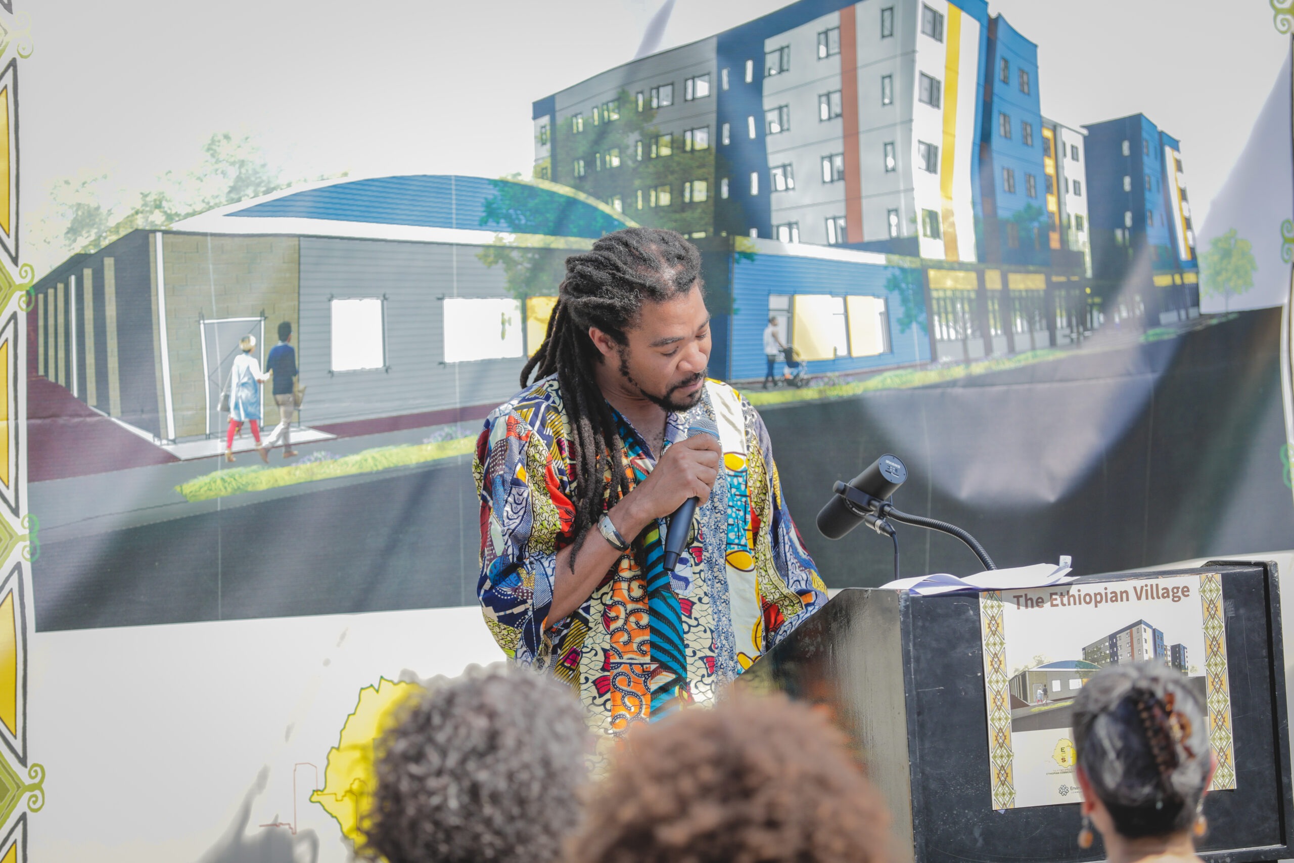 Man speaking into mic at a podium in front of building plans