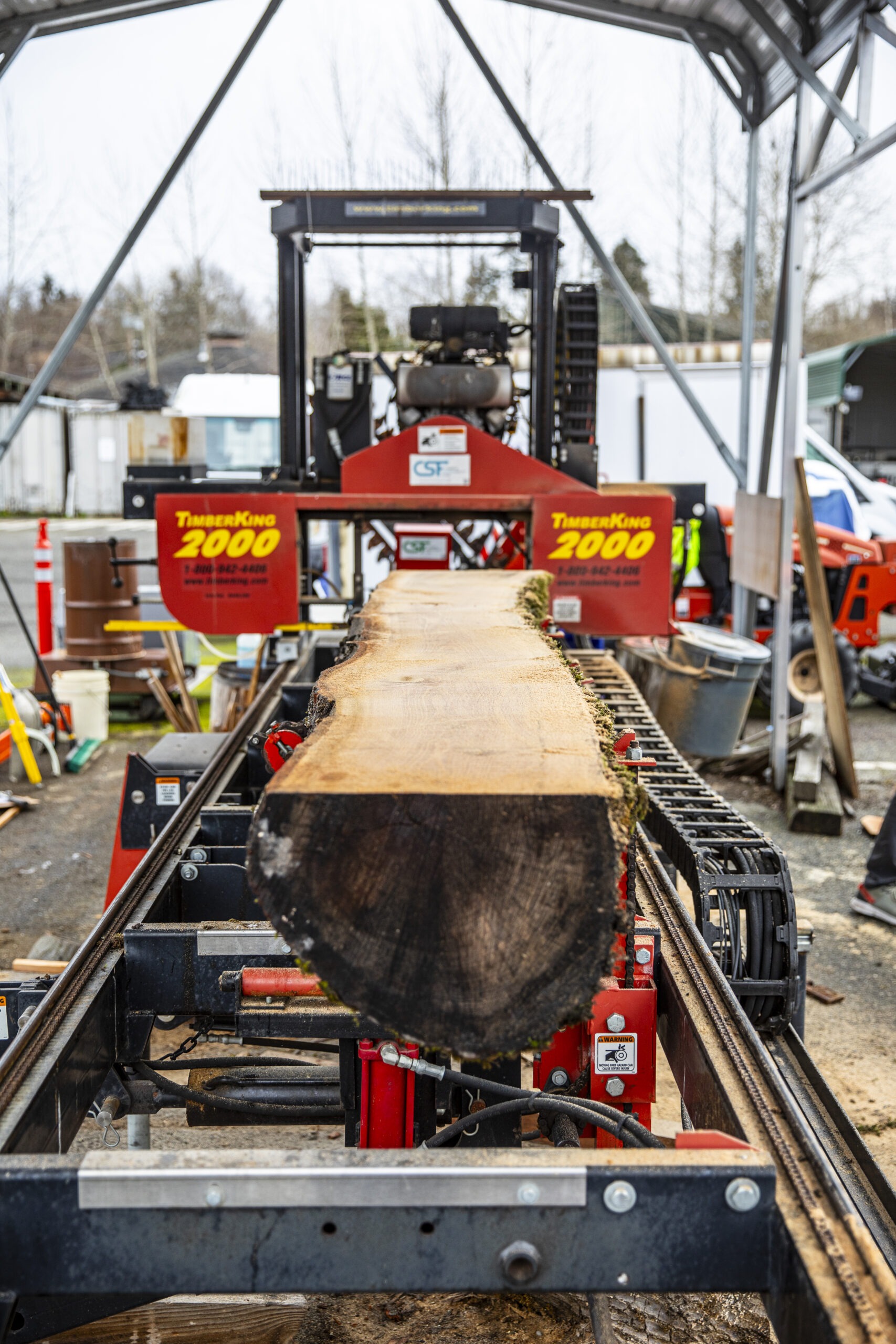 A wide view of the TimberKing 2000 sawmill in action, with a large log being milled into a plank under a metal canopy.