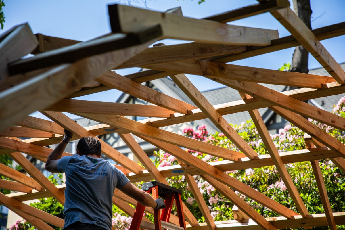 Student on ladder underneath interlaced wood that forms an arc