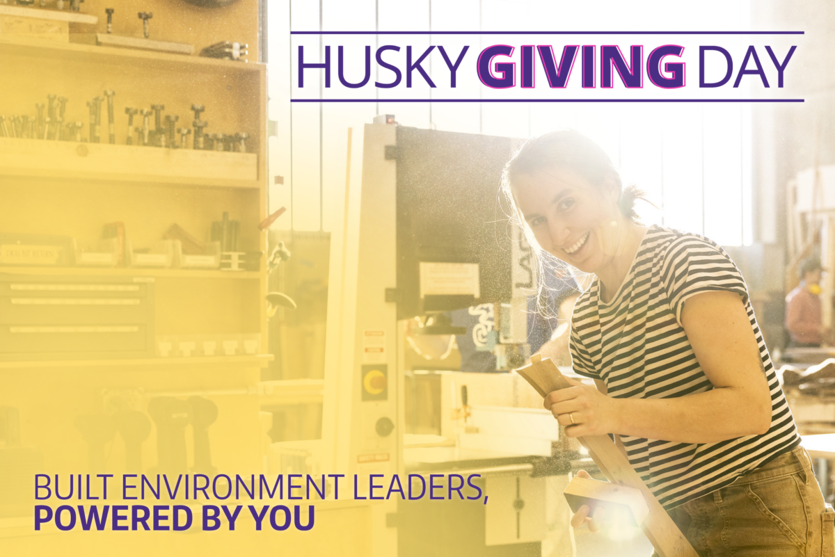 Student works with wood in a workshop, smiling toward the camera, with text overlay reading “Husky Giving Day: Built Environment Leaders, Powered by You.”