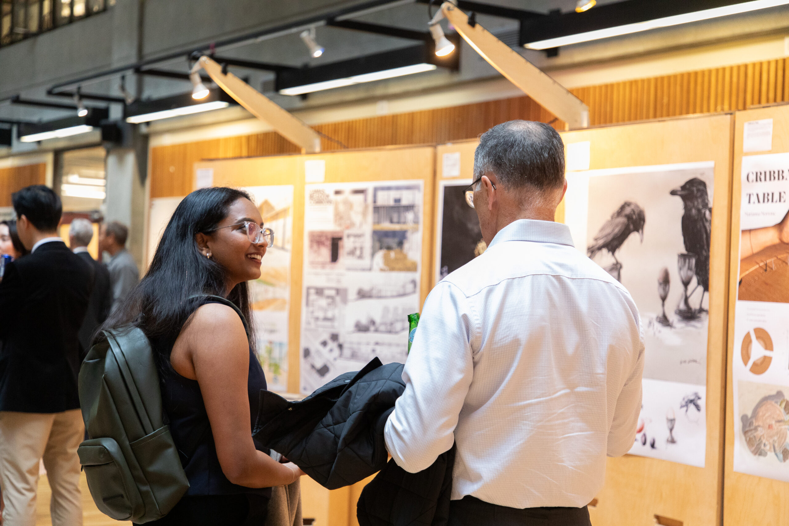 An attendee and guest stand in conversation while viewing architecture and design boards displayed at the exhibition.