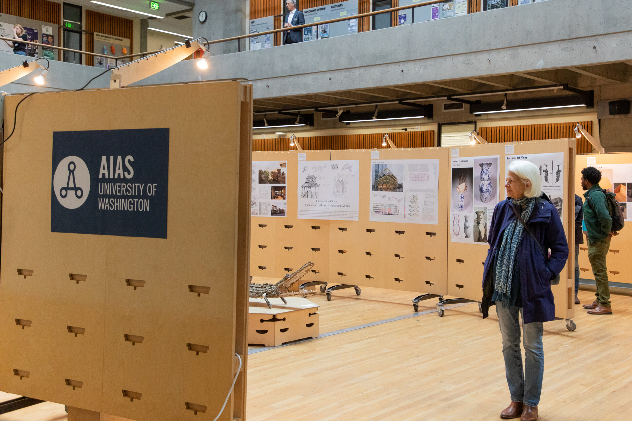 A visitor stands near an AIAS University of Washington display while viewing student work throughout the FrameWorks exhibition space in Gould Hall.